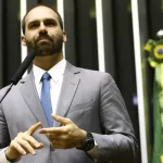Eduardo Bolsonaro durante evento político, com bandeira do Brasil ao fundo
