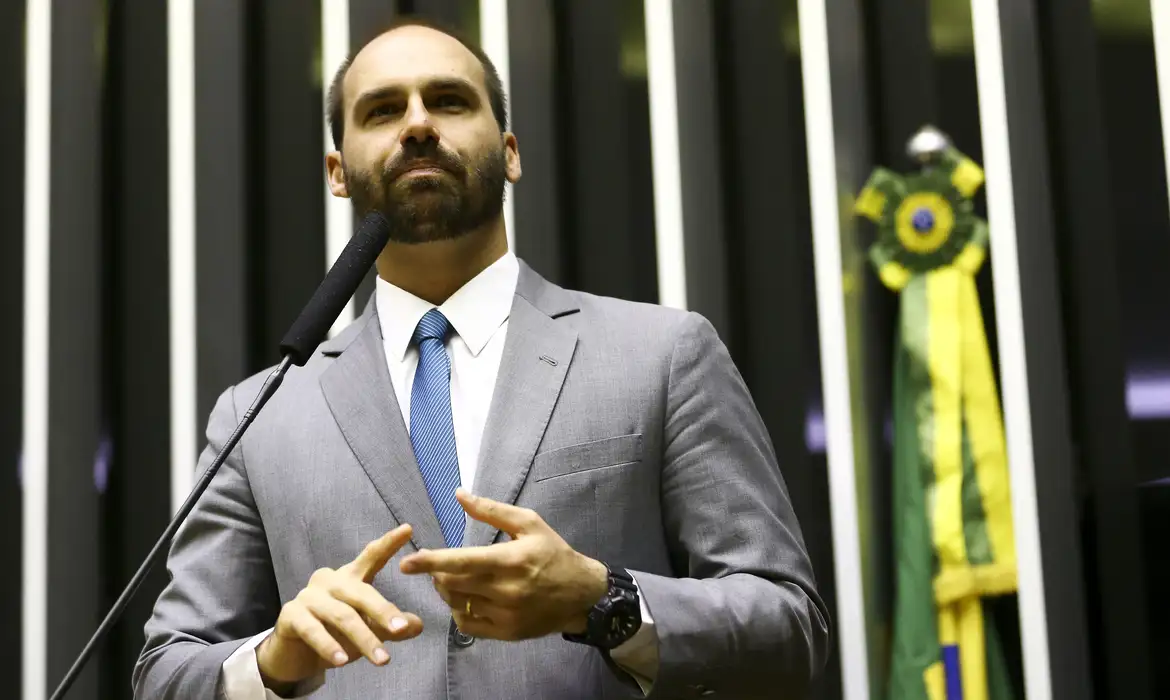 Eduardo Bolsonaro durante evento político, com bandeira do Brasil ao fundo