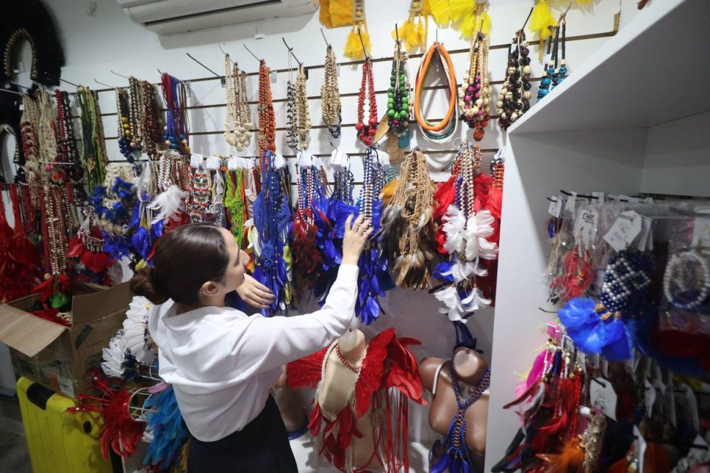 Turistas observam artesanato sustentável em barraca no Festival de Parintins, com destaque para biojoias sem uso de penas naturais.