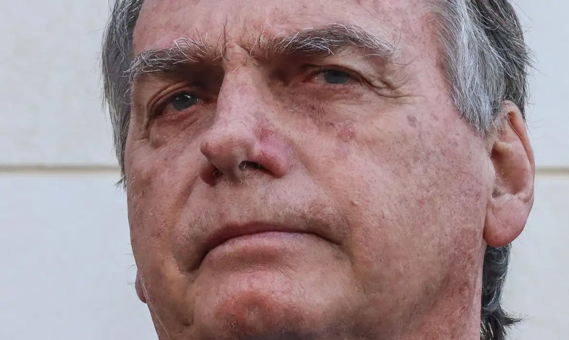 Jair Bolsonaro com expressão séria, destaque para tornozeleira eletrônica e fundo institucional
